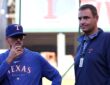 Rangers pitching coach Mike Maddux stands with his hand to his chin alongside executive Chris Young on the field.