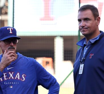 Rangers pitching coach Mike Maddux stands with his hand to his chin alongside executive Chris Young on the field.