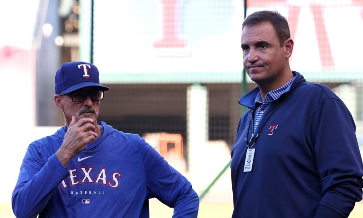 Rangers pitching coach Mike Maddux stands with his hand to his chin alongside executive Chris Young on the field.