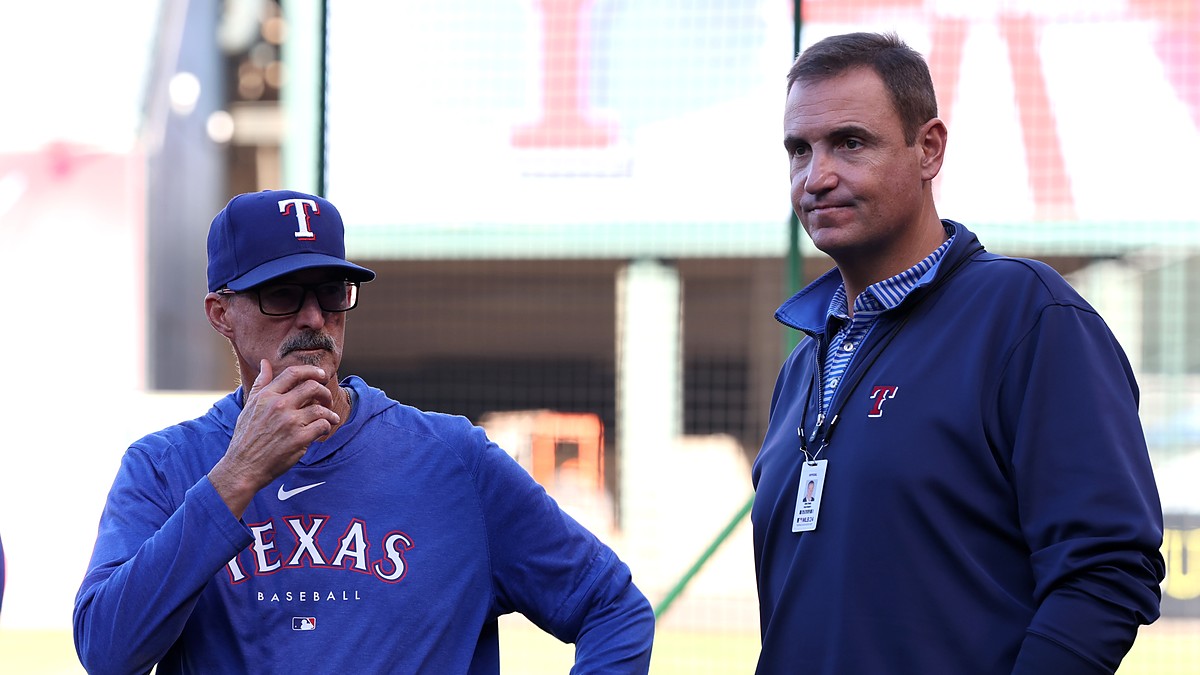 Rangers pitching coach Mike Maddux stands with his hand to his chin alongside executive Chris Young on the field.