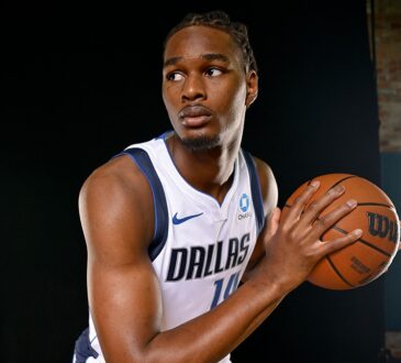Dallas Mavericks forward Morez Johnson Jr. holds a basketball and looks to his right in a white home jersey.