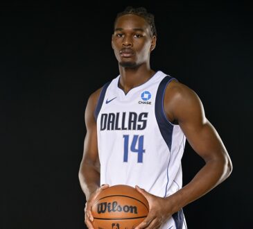 Dallas Mavericks forward Morez Johnson Jr. poses with a basketball in a white home jersey against a black backdrop.