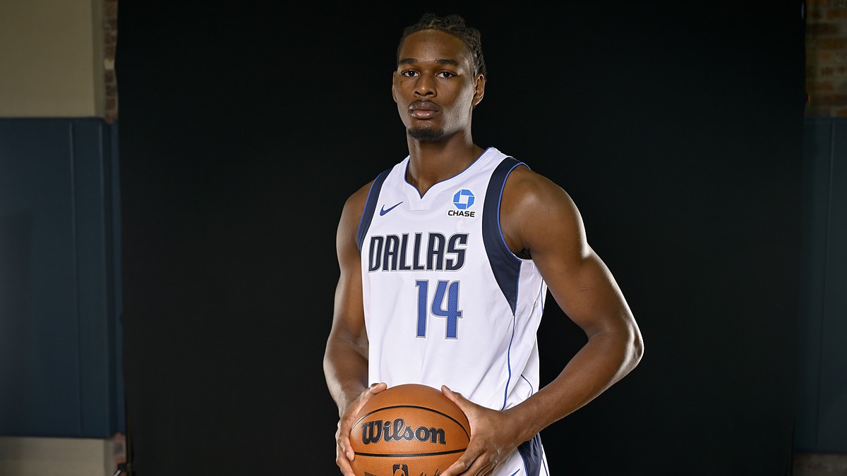 Dallas Mavericks forward Morez Johnson Jr. poses with a basketball in a white home jersey against a black backdrop.