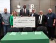 Myles Turner holds an oversized $2 million check flanked by eight district officials at a board meeting.