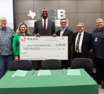Myles Turner holds an oversized $2 million check flanked by eight district officials at a board meeting.