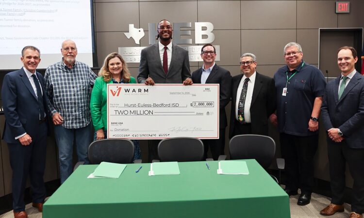 Myles Turner holds an oversized $2 million check flanked by eight district officials at a board meeting.