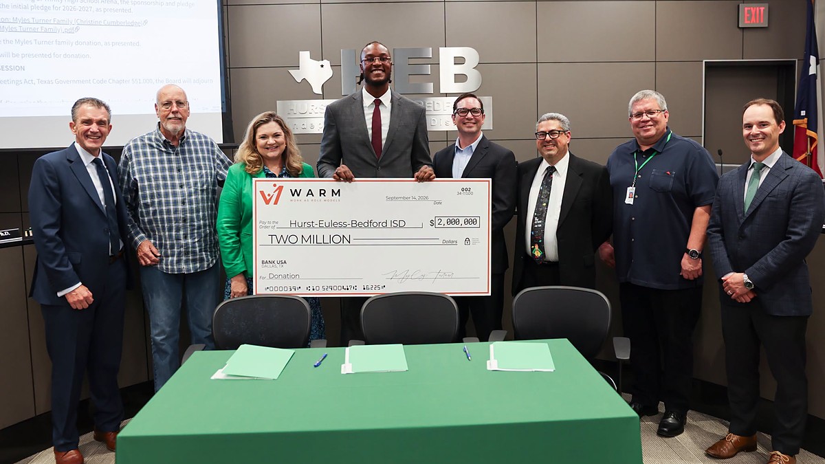 Myles Turner holds an oversized $2 million check flanked by eight district officials at a board meeting.