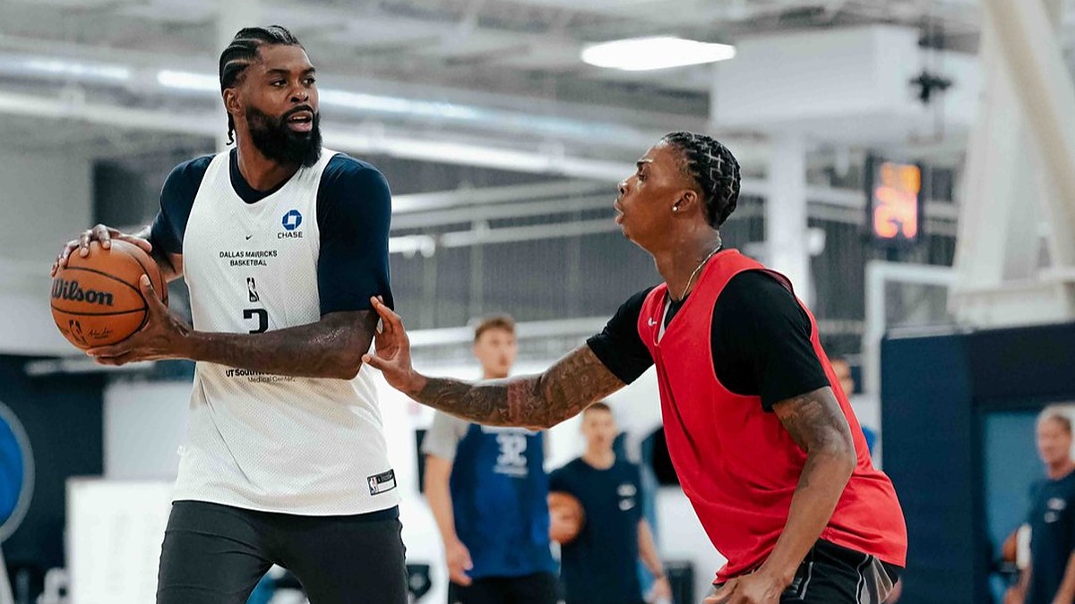 Dallas Mavericks forward Naji Marshall holds the ball as a teammate in a red practice jersey defends him.