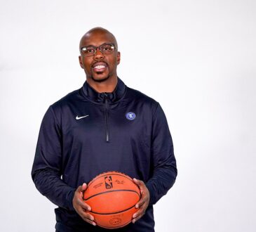 Texas Legends head coach Nathaniel Mitchell smiles and holds a basketball with both hands during a studio portrait.