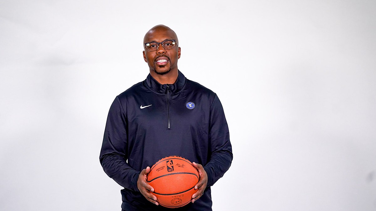 Texas Legends head coach Nathaniel Mitchell smiles and holds a basketball with both hands during a studio portrait.