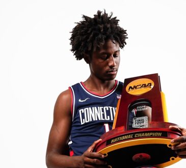 Guard NaVorro Bowman Jr. sits in a Connecticut uniform holding the NCAA national championship trophy.