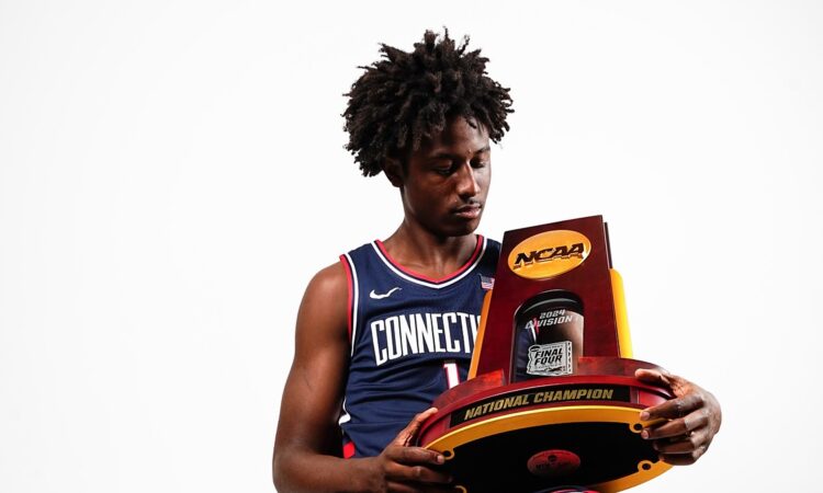 Guard NaVorro Bowman Jr. sits in a Connecticut uniform holding the NCAA national championship trophy.