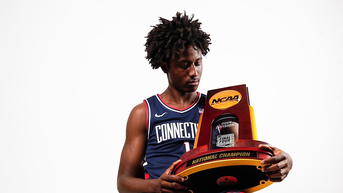Guard NaVorro Bowman Jr. sits in a Connecticut uniform holding the NCAA national championship trophy.