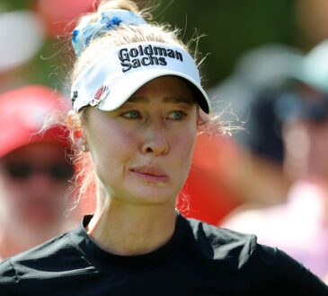 Golfer Nelly Korda, in a white visor and black top, looks to the side while waiting to hit.