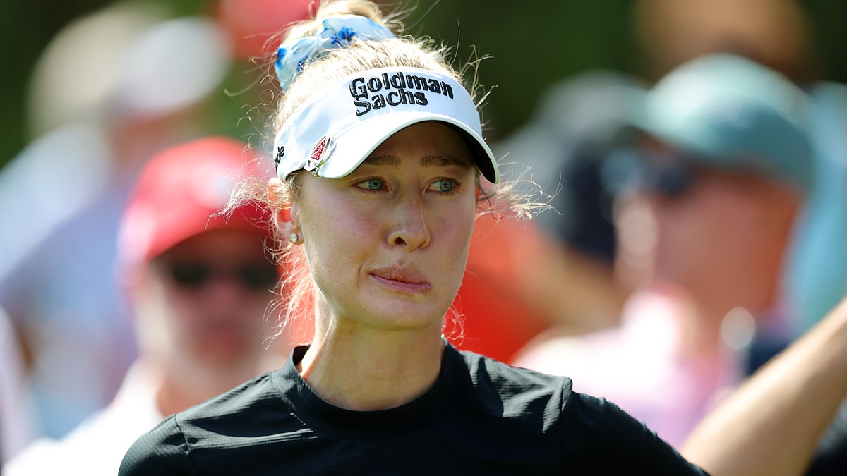 Golfer Nelly Korda, in a white visor and black top, looks to the side while waiting to hit.