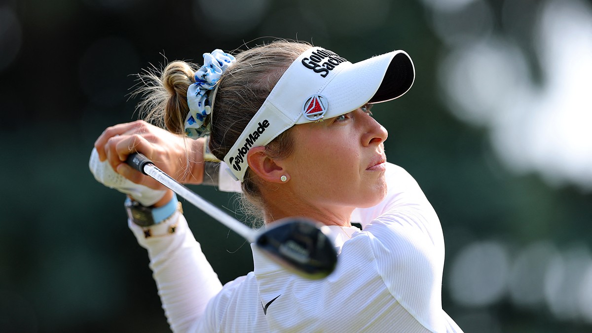 Golfer Nelly Korda watches her tee shot after swinging, wearing a white visor and a blue floral scrunchie.
