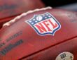 A close view of the NFL shield stamped on a Wilson game football resting alongside another ball.