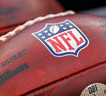 A close view of the NFL shield stamped on a Wilson game football resting alongside another ball.