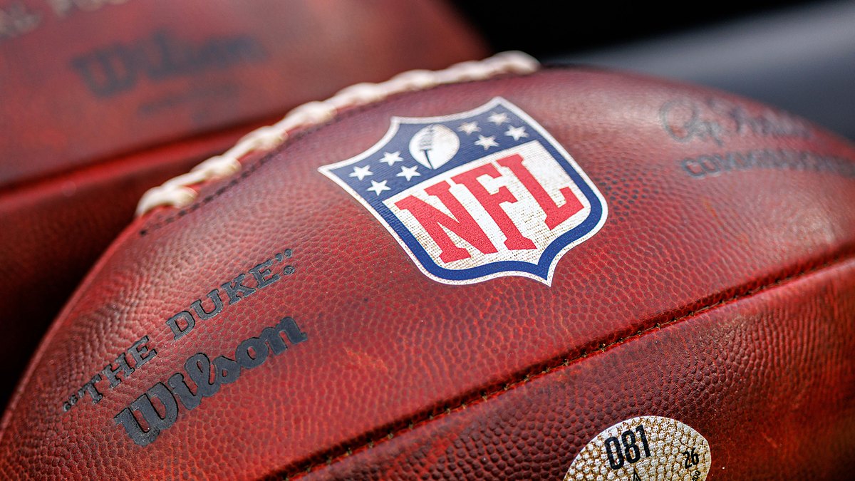 A close view of the NFL shield stamped on a Wilson game football resting alongside another ball.