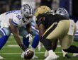 Dallas Cowboys guard Nick Leverett grips the ball in a three-point stance across the line from a New Orleans Saints defender.
