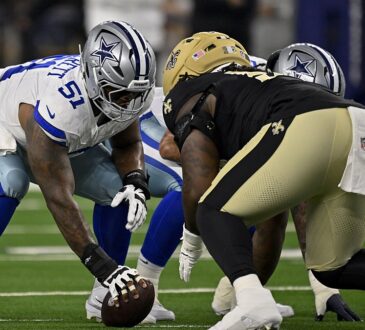 Dallas Cowboys guard Nick Leverett grips the ball in a three-point stance across the line from a New Orleans Saints defender.