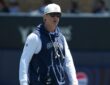 Dallas Cowboys special teams coordinator Nick Sorensen watches a training camp practice in a team hoodie and cap.