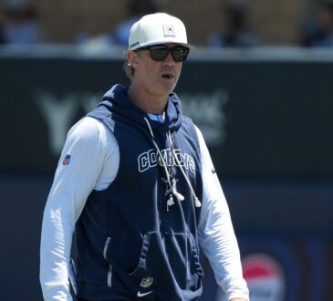 Dallas Cowboys special teams coordinator Nick Sorensen watches a training camp practice in a team hoodie and cap.