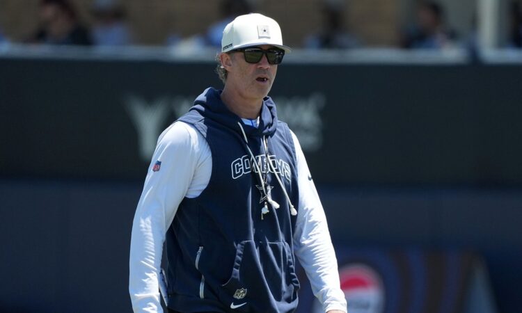 Dallas Cowboys special teams coordinator Nick Sorensen watches a training camp practice in a team hoodie and cap.
