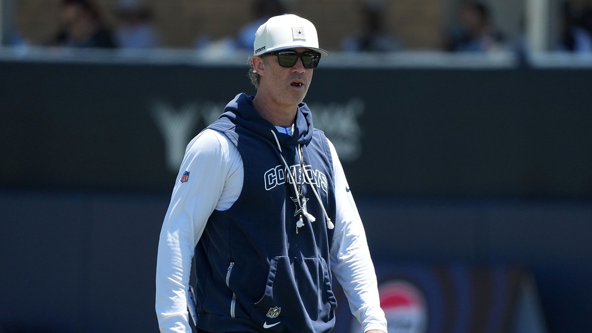 Dallas Cowboys special teams coordinator Nick Sorensen watches a training camp practice in a team hoodie and cap.