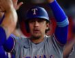Texas Rangers infielder Nicky Lopez raises his arms as teammates greet him in the dugout after he scores a run.