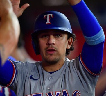 Texas Rangers infielder Nicky Lopez raises his arms as teammates greet him in the dugout after he scores a run.