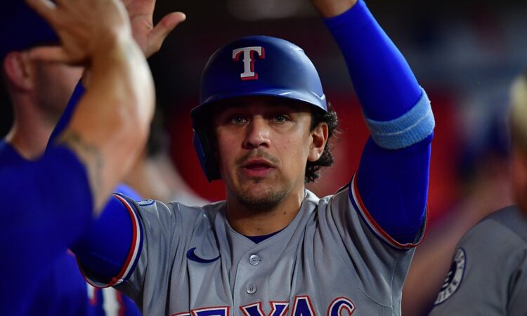 Texas Rangers infielder Nicky Lopez raises his arms as teammates greet him in the dugout after he scores a run.