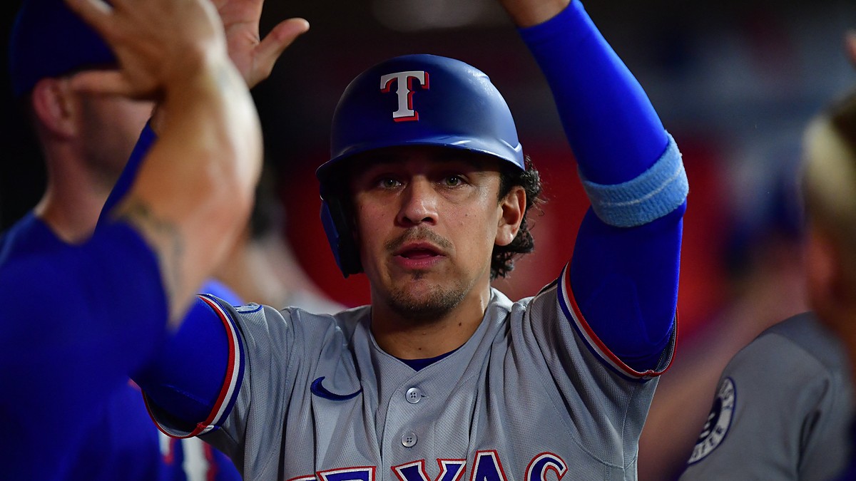Texas Rangers infielder Nicky Lopez raises his arms as teammates greet him in the dugout after he scores a run.