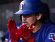 Texas Rangers second baseman Nicky Lopez claps his red batting gloves together in the dugout.