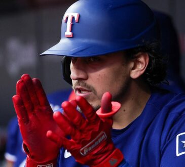 Texas Rangers second baseman Nicky Lopez claps his red batting gloves together in the dugout.