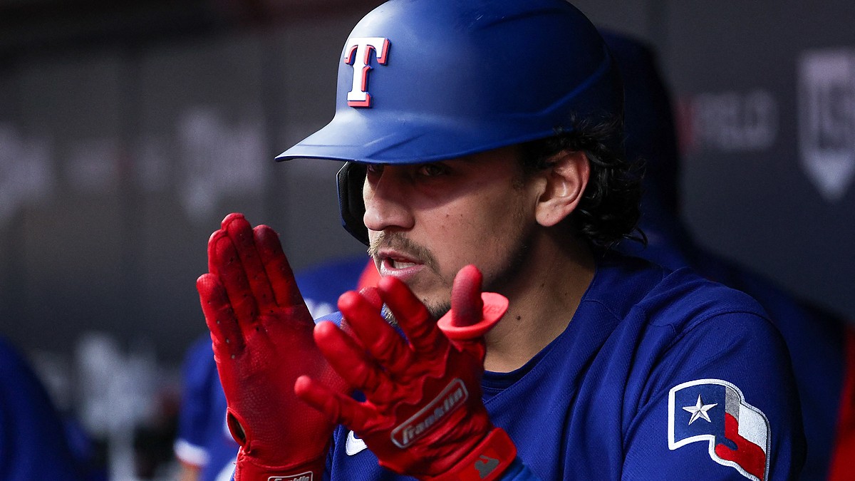 Texas Rangers second baseman Nicky Lopez claps his red batting gloves together in the dugout.