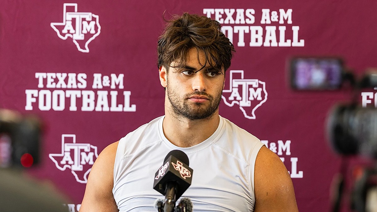 Texas A&M's Noah Mikhail sits in front of a Texas A&M Football backdrop while speaking to reporters.