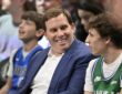Mavericks governor Patrick Dumont smiles in a blue jacket while sitting courtside among fans.
