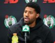 Celtics forward Paul George speaks into a microphone at a podium backed by Celtics logos.