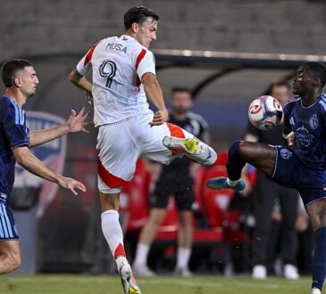 FC Dallas forward Petar Musa leaps for the ball as two Sporting Kansas City players challenge him.