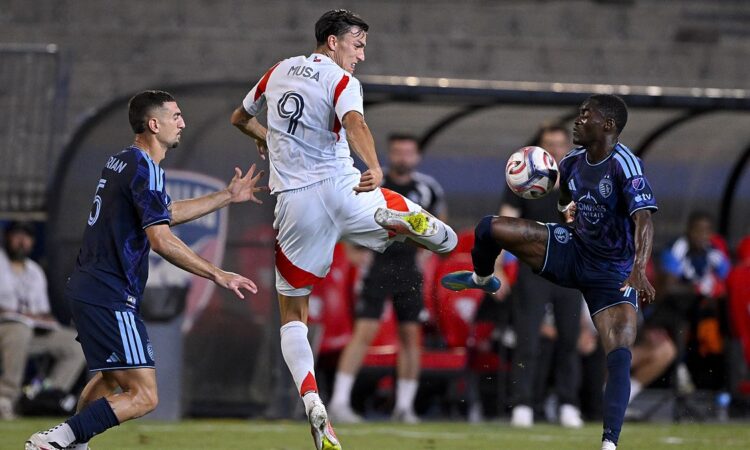 FC Dallas forward Petar Musa leaps for the ball as two Sporting Kansas City players challenge him.