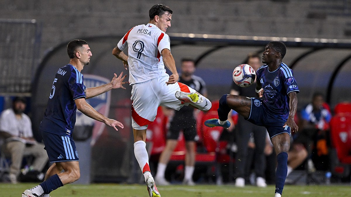 FC Dallas forward Petar Musa leaps for the ball as two Sporting Kansas City players challenge him.