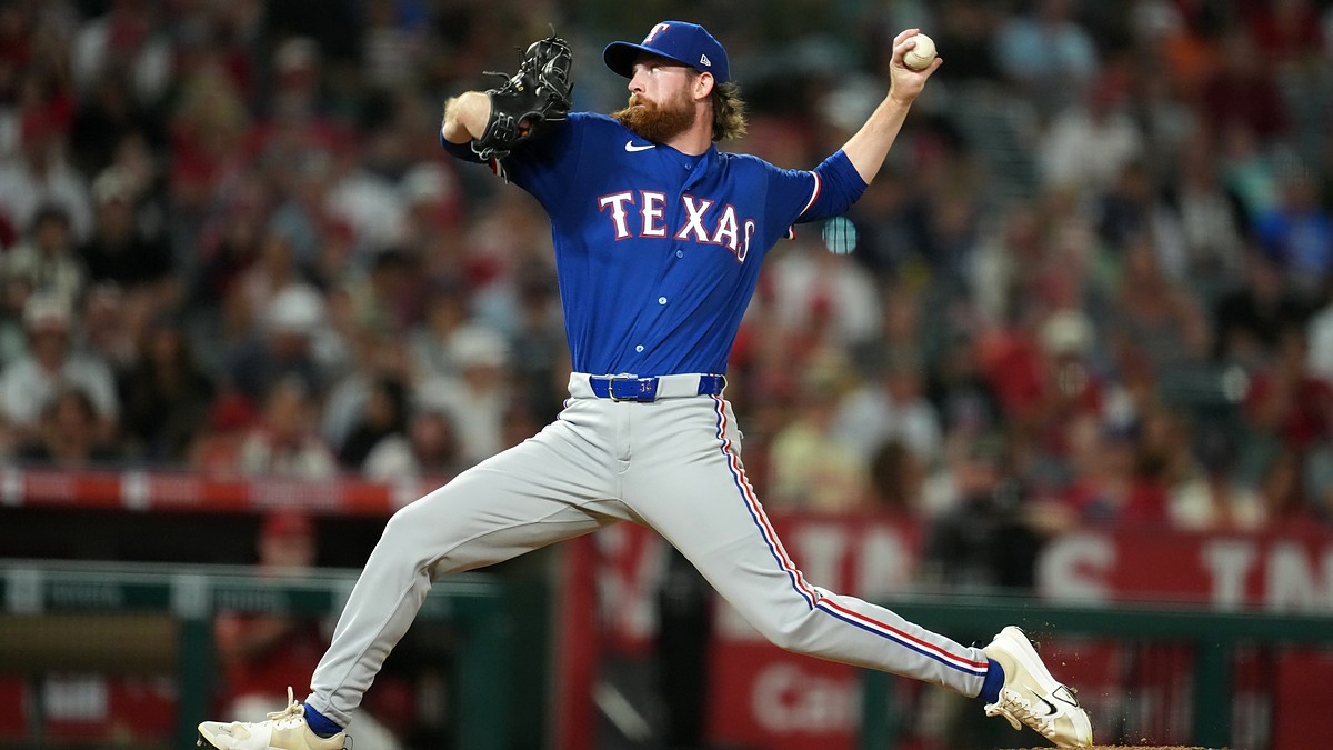 Texas Rangers pitcher Peyton Gray strides toward the plate mid-delivery in a road gray uniform.