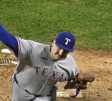 Texas Rangers pitcher Peyton Gray, seen from above, extends his arm back to throw from the mound in his road uniform.
