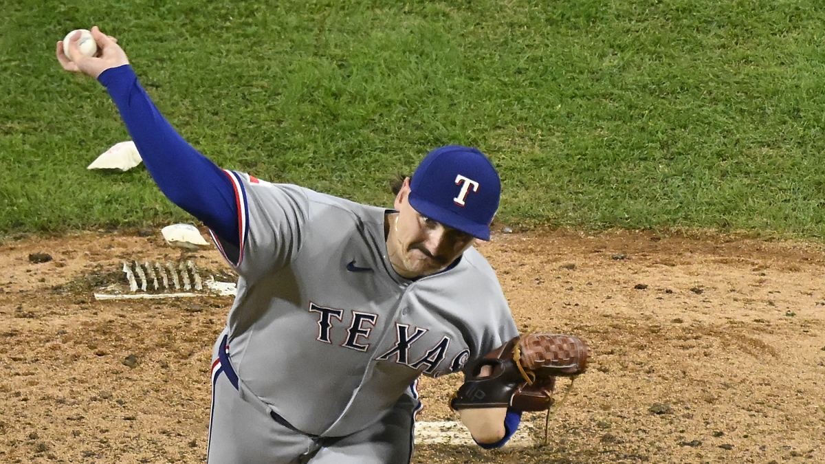 Texas Rangers pitcher Peyton Gray, seen from above, extends his arm back to throw from the mound in his road uniform.