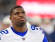 Dallas Cowboys defensive tackle Quinnen Williams gazes upward on the sideline with a blurred video board behind him.