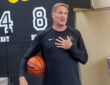 Miami Heat shooting coach Rob Fodor holds a basketball under his arm and speaks with his hand on his chest.