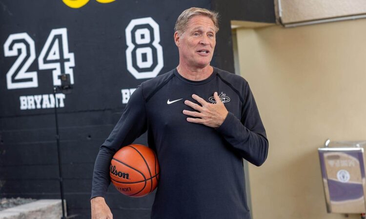 Miami Heat shooting coach Rob Fodor holds a basketball under his arm and speaks with his hand on his chest.