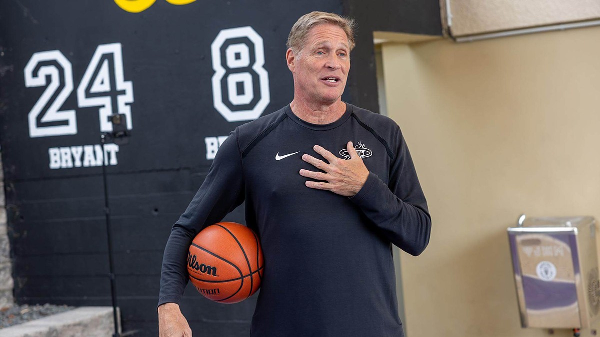 Miami Heat shooting coach Rob Fodor holds a basketball under his arm and speaks with his hand on his chest.