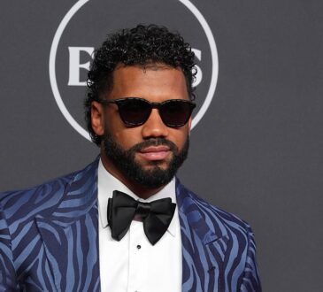 Russell Wilson poses in a patterned blue tuxedo jacket and sunglasses on the ESPY Awards red carpet.
